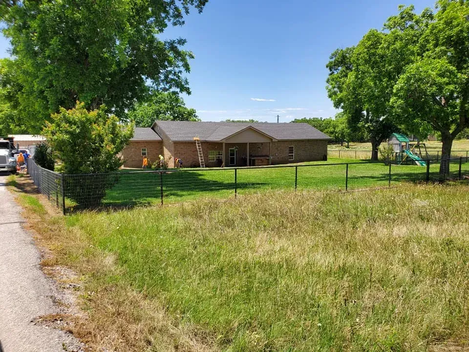 A one-story brick house with a covered patio and a fenced yard on a sunny day.