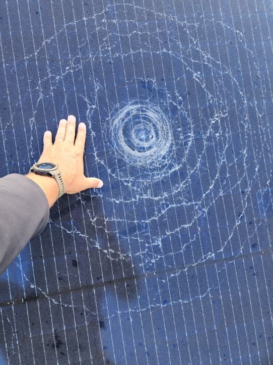 Hand on a cracked solar panel, showing a circular crack pattern radiating outwards.