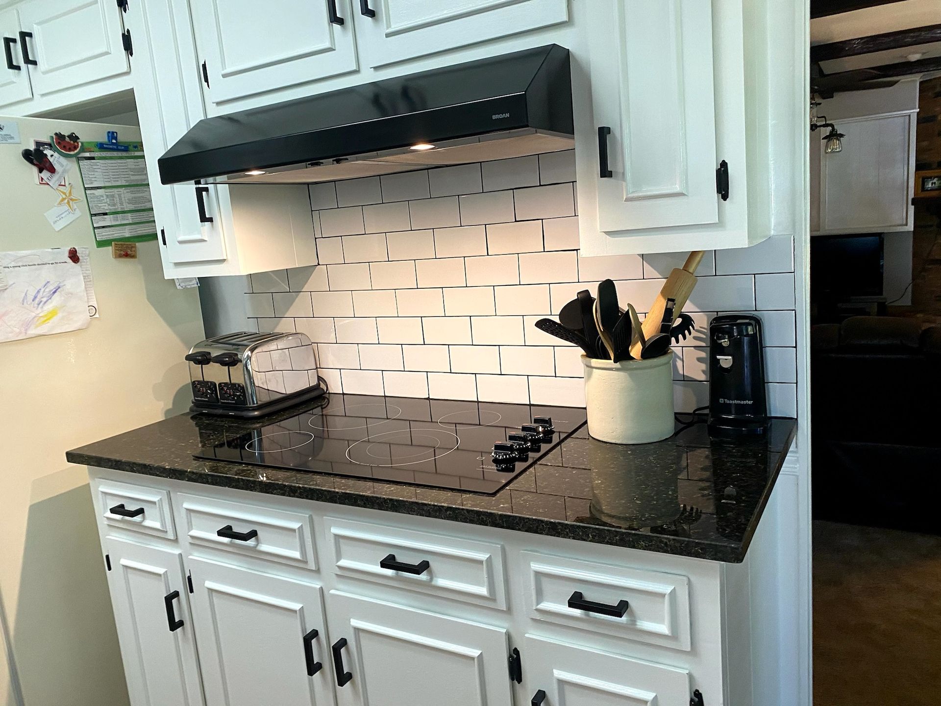 White kitchen with black countertop, cabinets, and backsplash. Includes appliances and utensils.