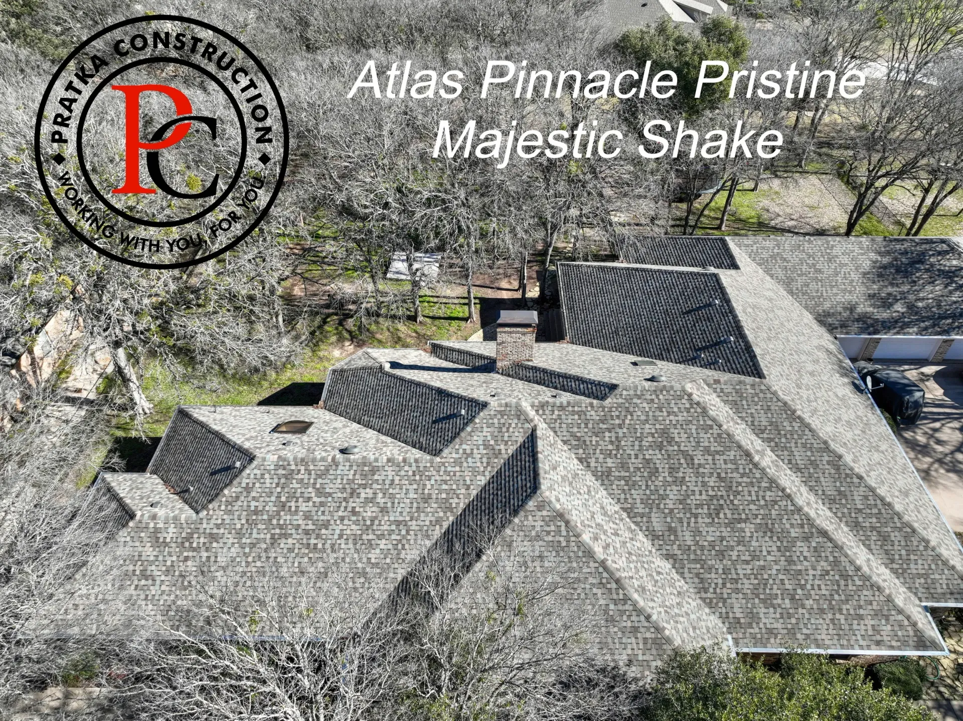 Aerial view of a roof with gray, textured shingles; trees surround the house.