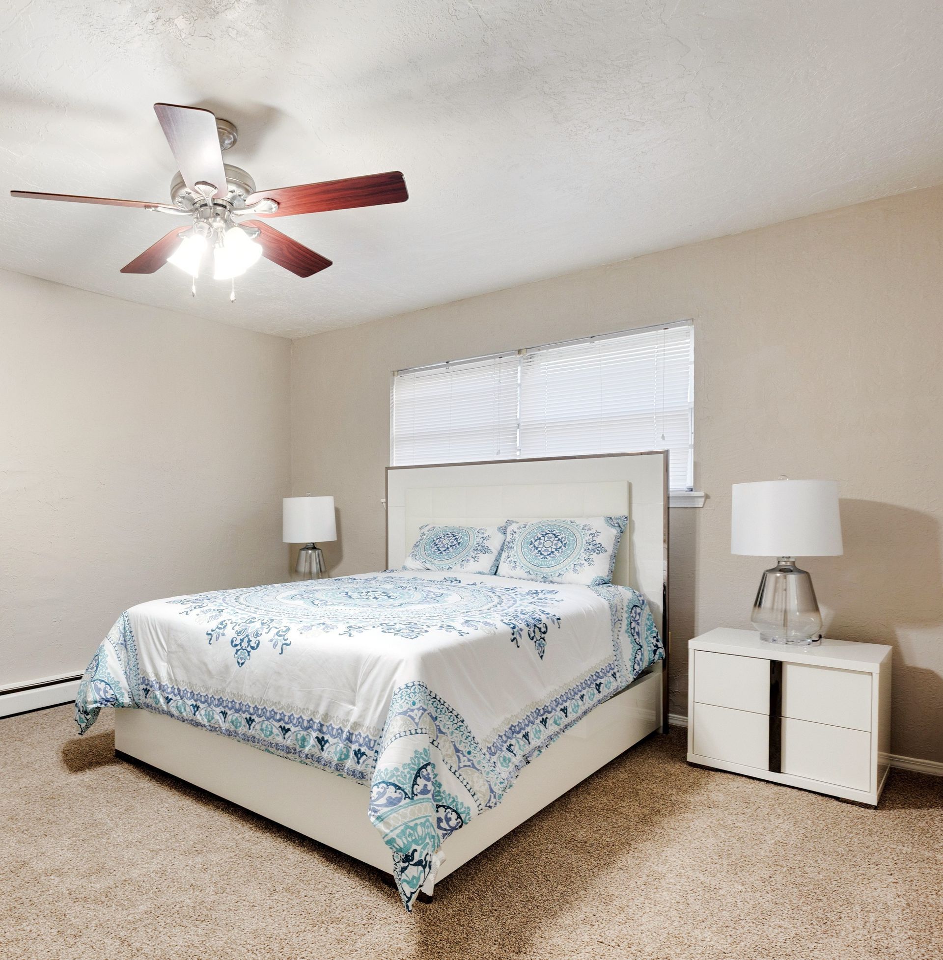 Bedroom with white bed, patterned bedding, two nightstands, and a ceiling fan.
