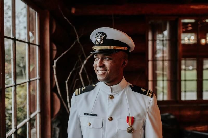 A man in a military uniform is standing in front of a window.