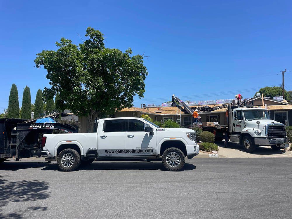 A white truck is parked in front of a house with a trailer attached to it.