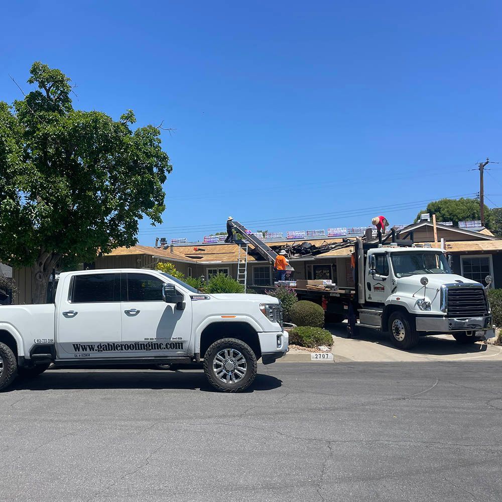 Two white trucks are parked in front of a house.