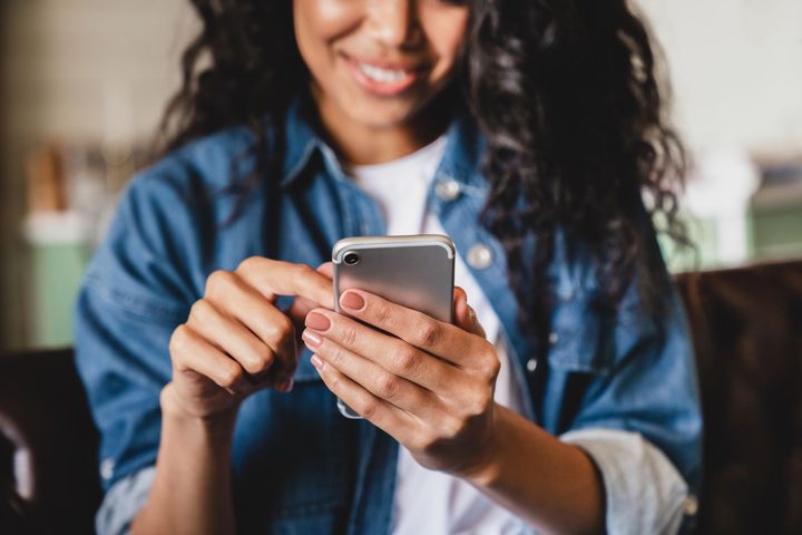 A woman is sitting on a couch using a cell phone.