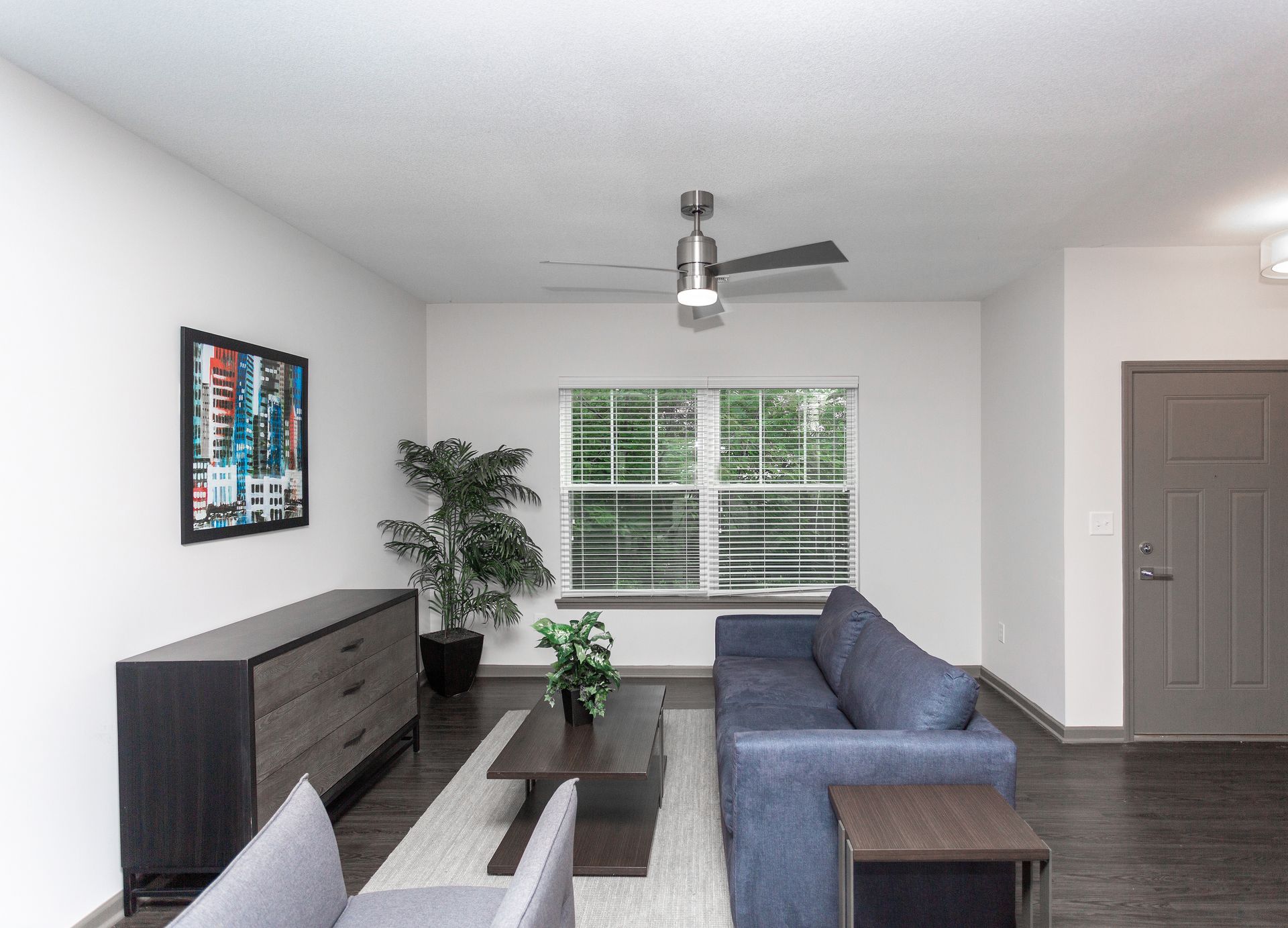 A living room with a couch , chairs , coffee table and ceiling fan.