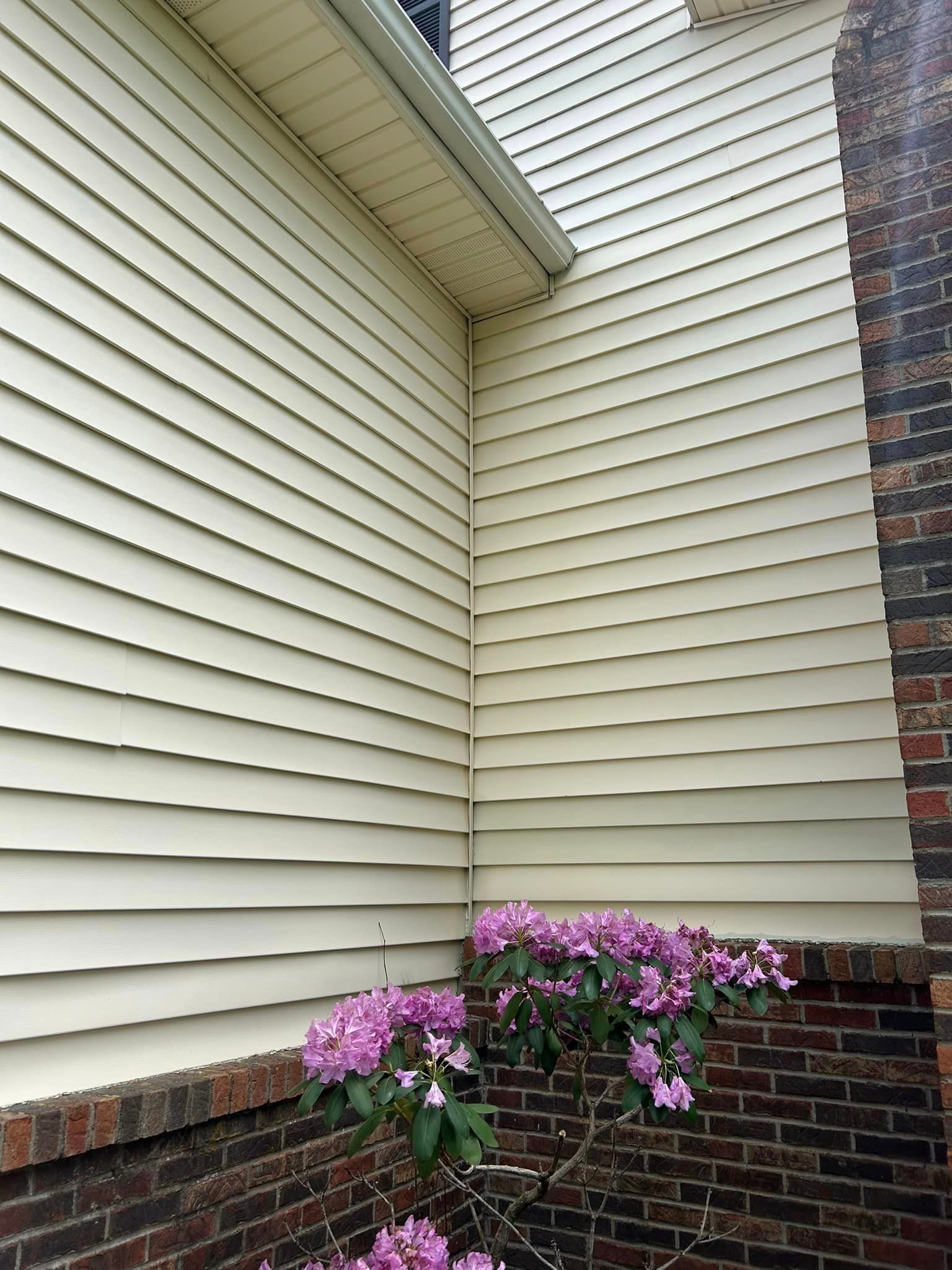 A white siding on the side of a house next to a brick wall with purple flowers.