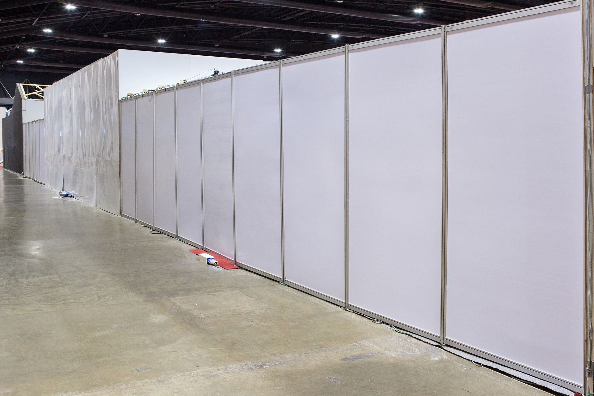 Long hallway with white booth walls, gray concrete floor, and dark ceiling.