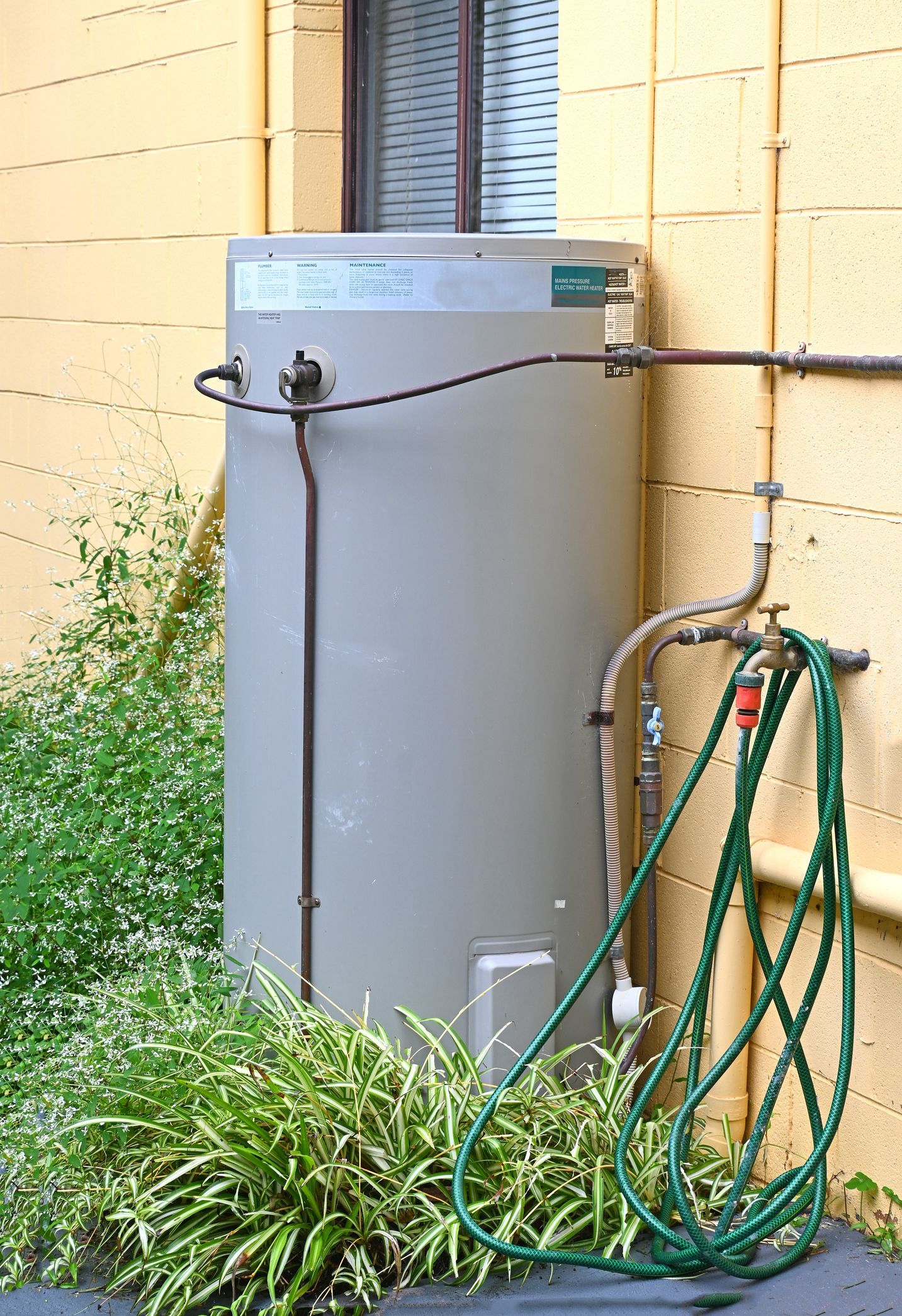 A gray water heater next to a yellow wall with a green hose coiled nearby.