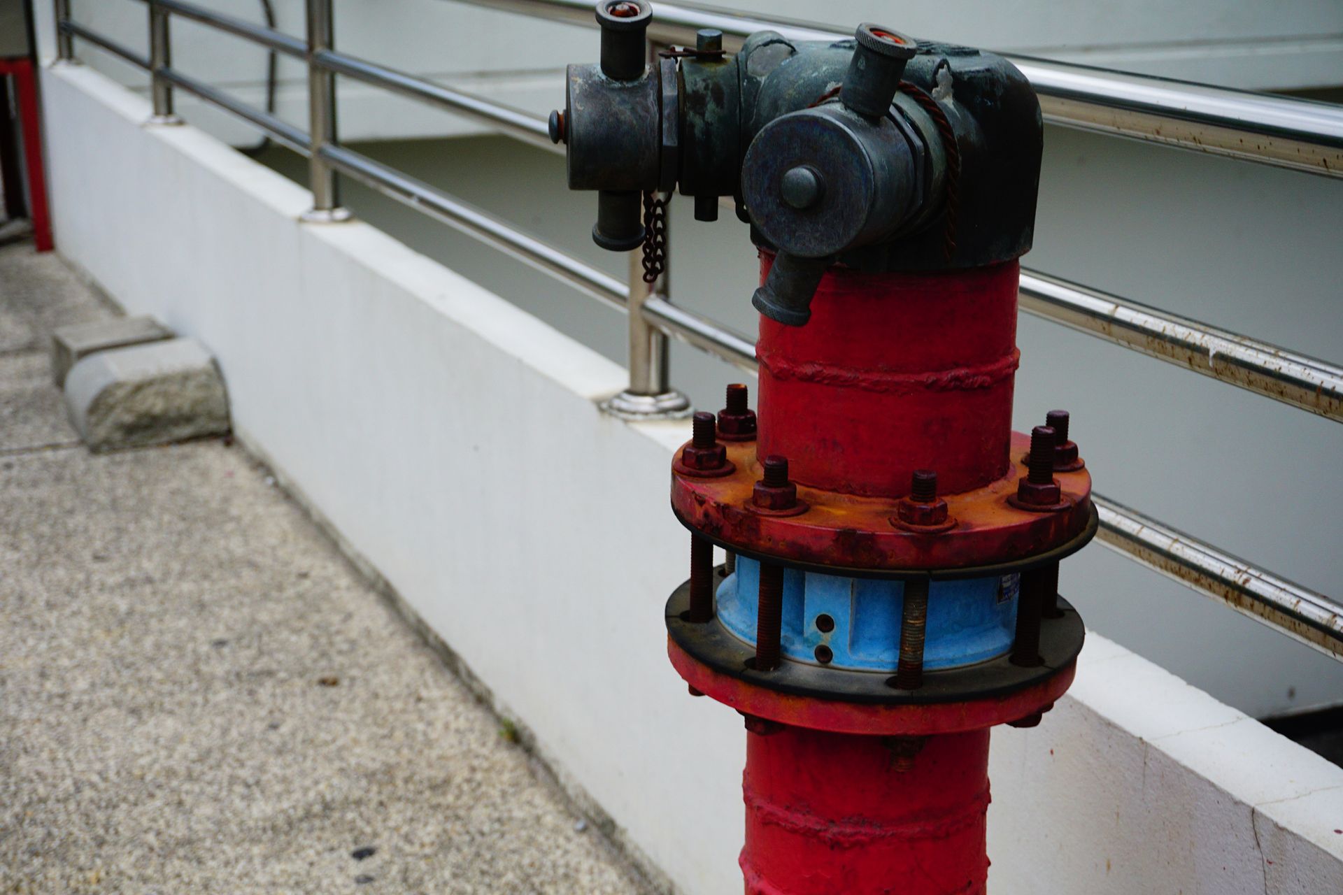 Red fire hydrant on a concrete surface, near a white wall and metal railing.