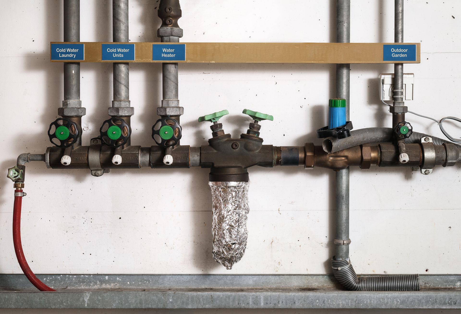 Pipes with valves and labels mounted on a white wall. Some pipes have green handles and filters.