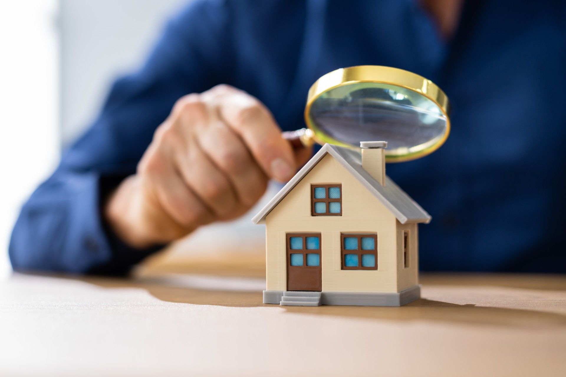 A person is looking at a model house with a magnifying glass.