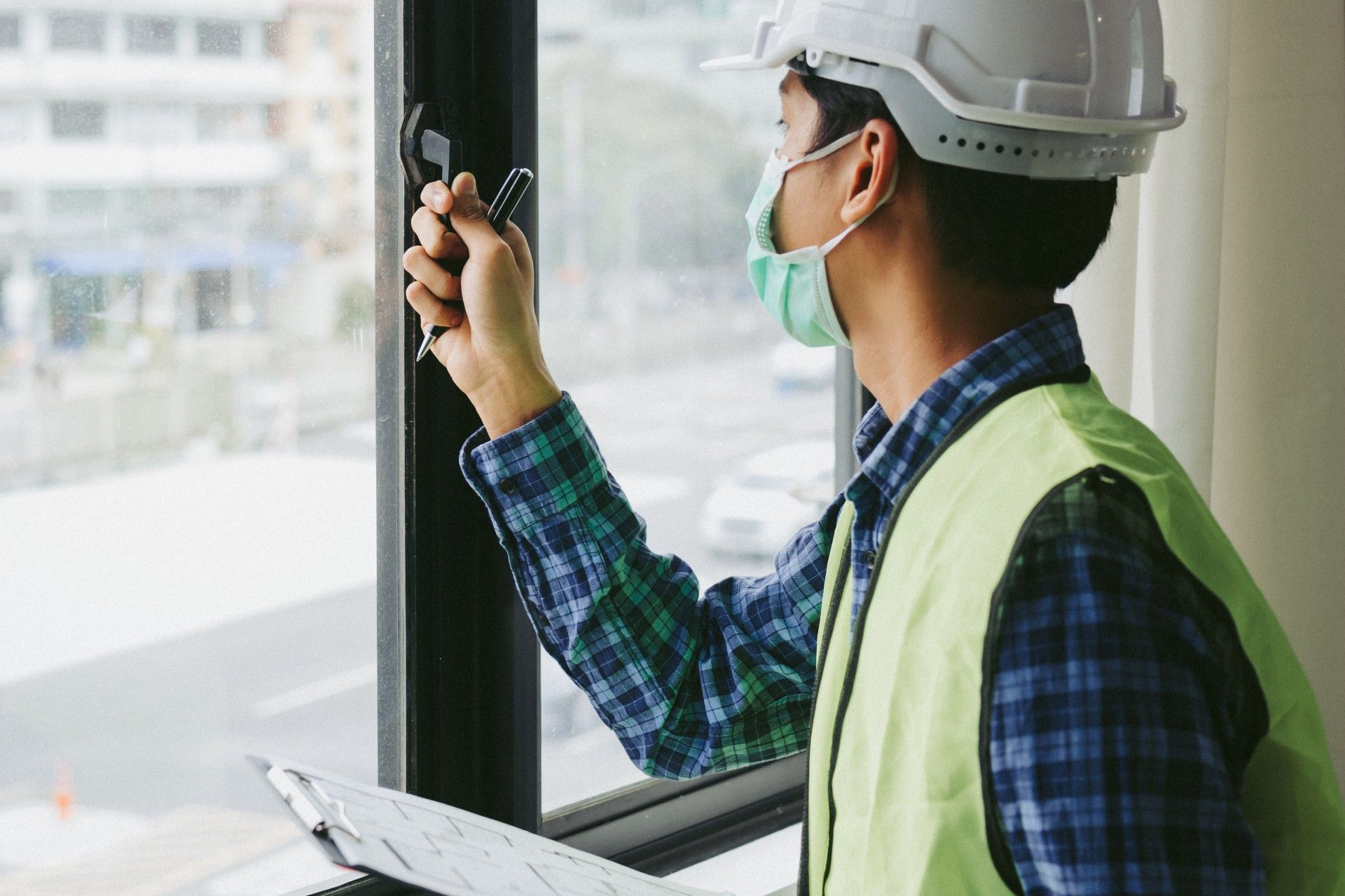 A man wearing a hard hat and safety vest is looking out of a window.