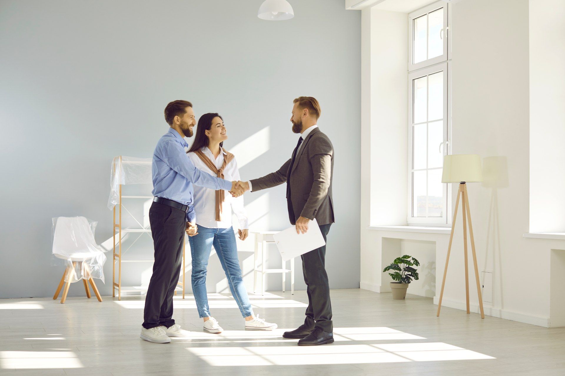 A man and woman are shaking hands with a real estate agent in an empty room.