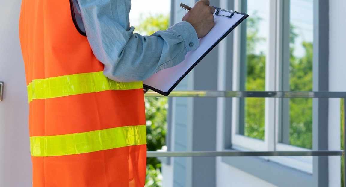 A man in an orange vest is holding a clipboard and writing on it.