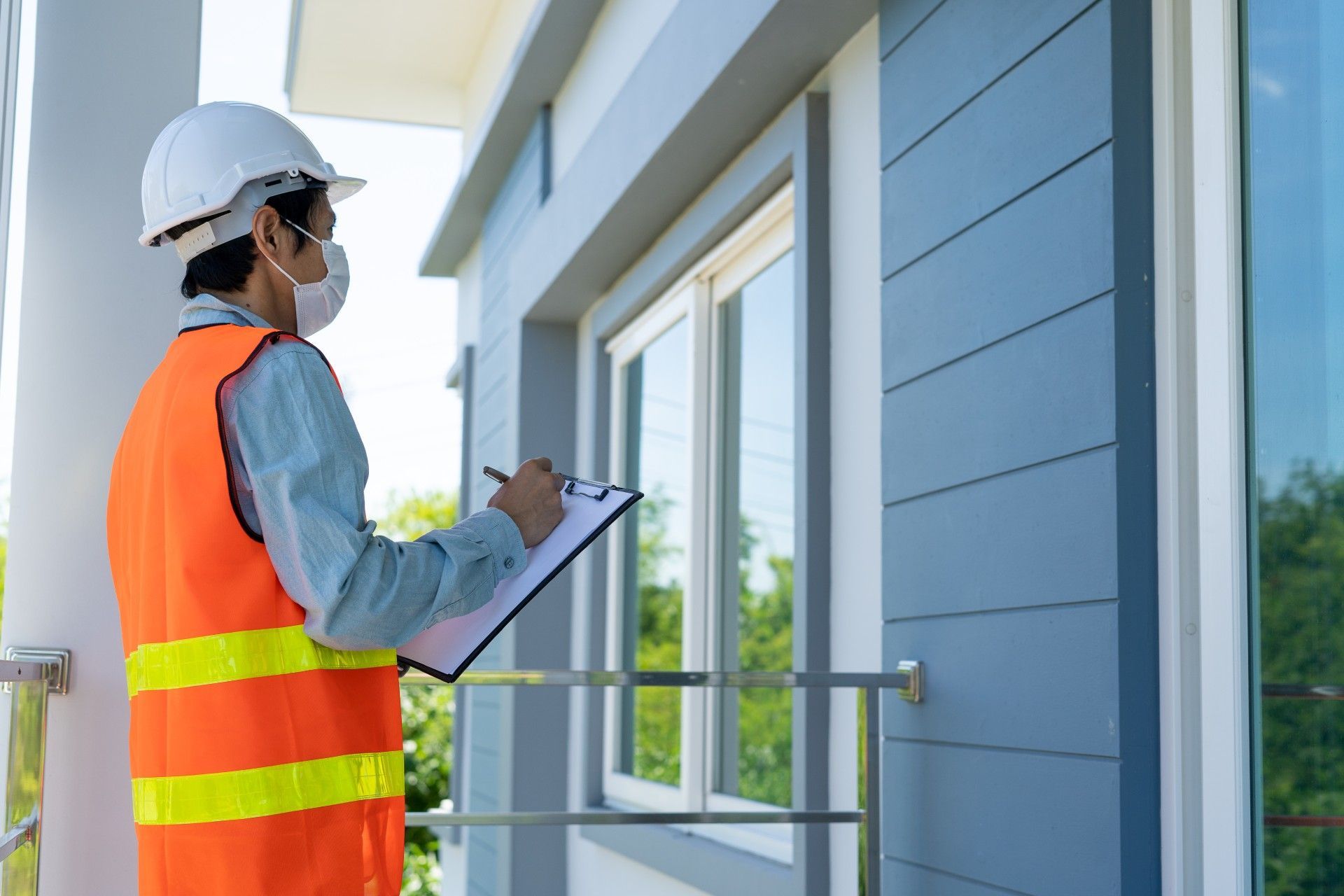 A man wearing a mask is standing in front of a building holding a clipboard.