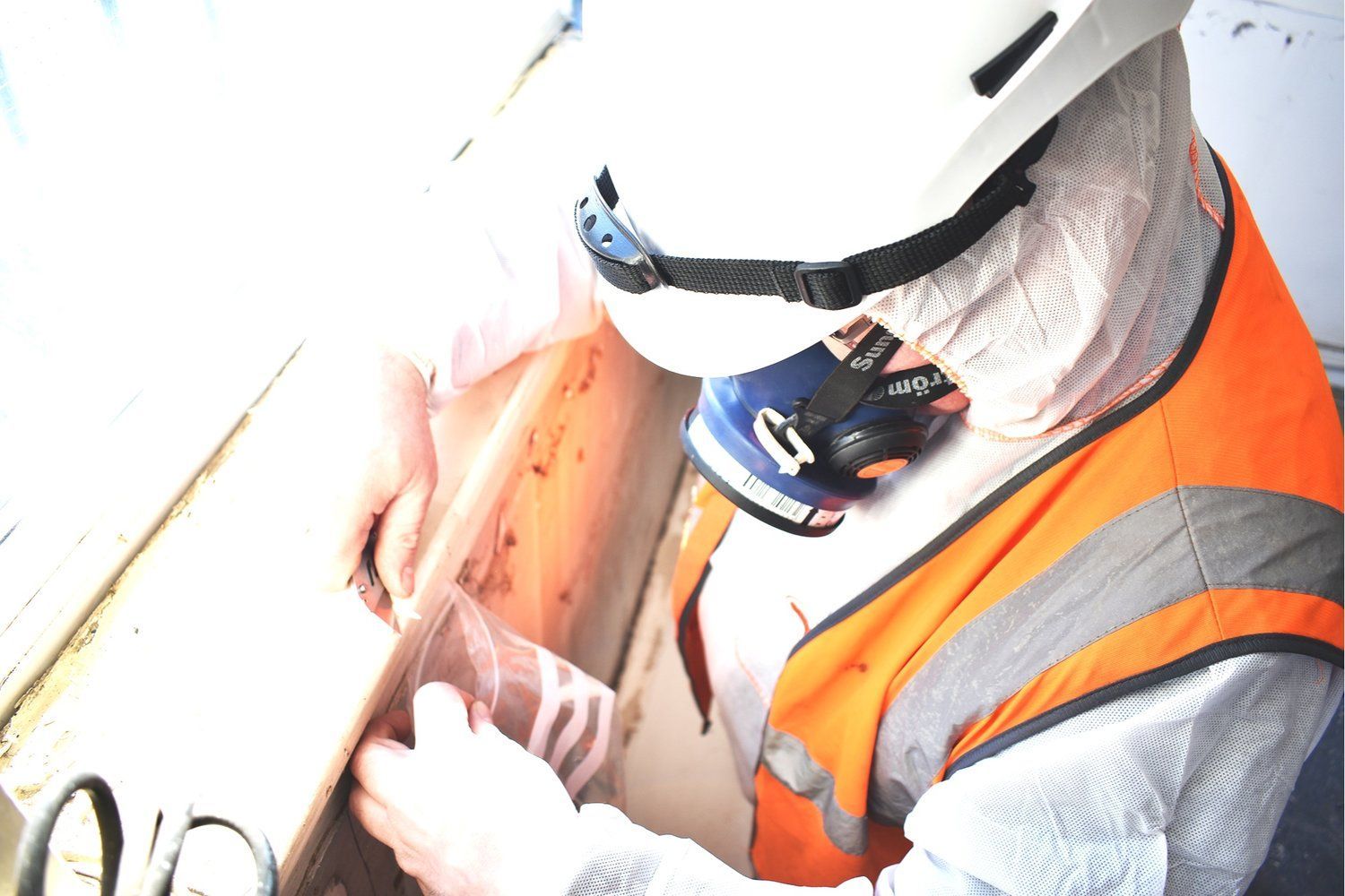 A man wearing a helmet and safety vest is working on a piece of wood.