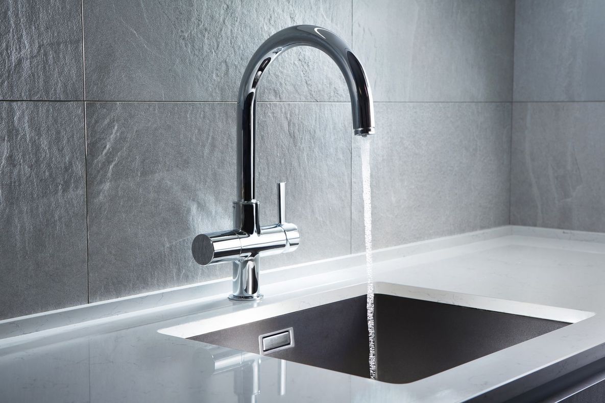 Chrome faucet with water running into a dark gray sink, against a gray tiled wall.