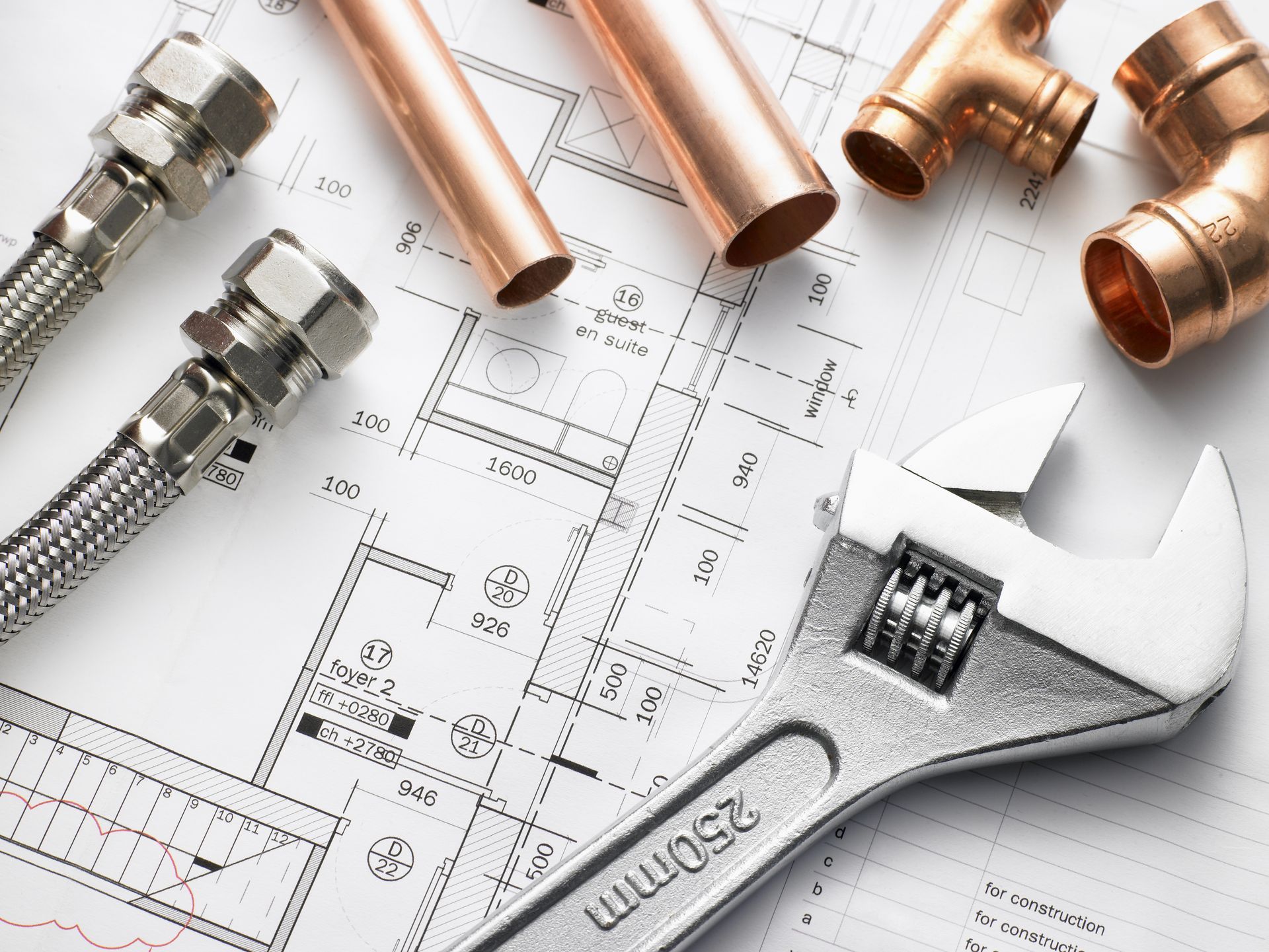 Plumbing tools and copper pipes on architectural plans; wrench, fittings, hoses.