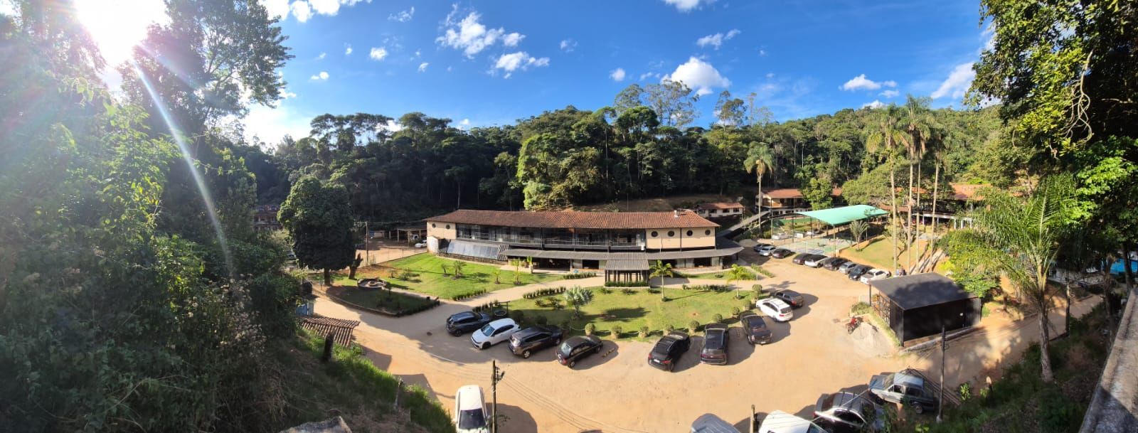 Um grande edifício com muitos carros estacionados em frente, cercado por árvores.