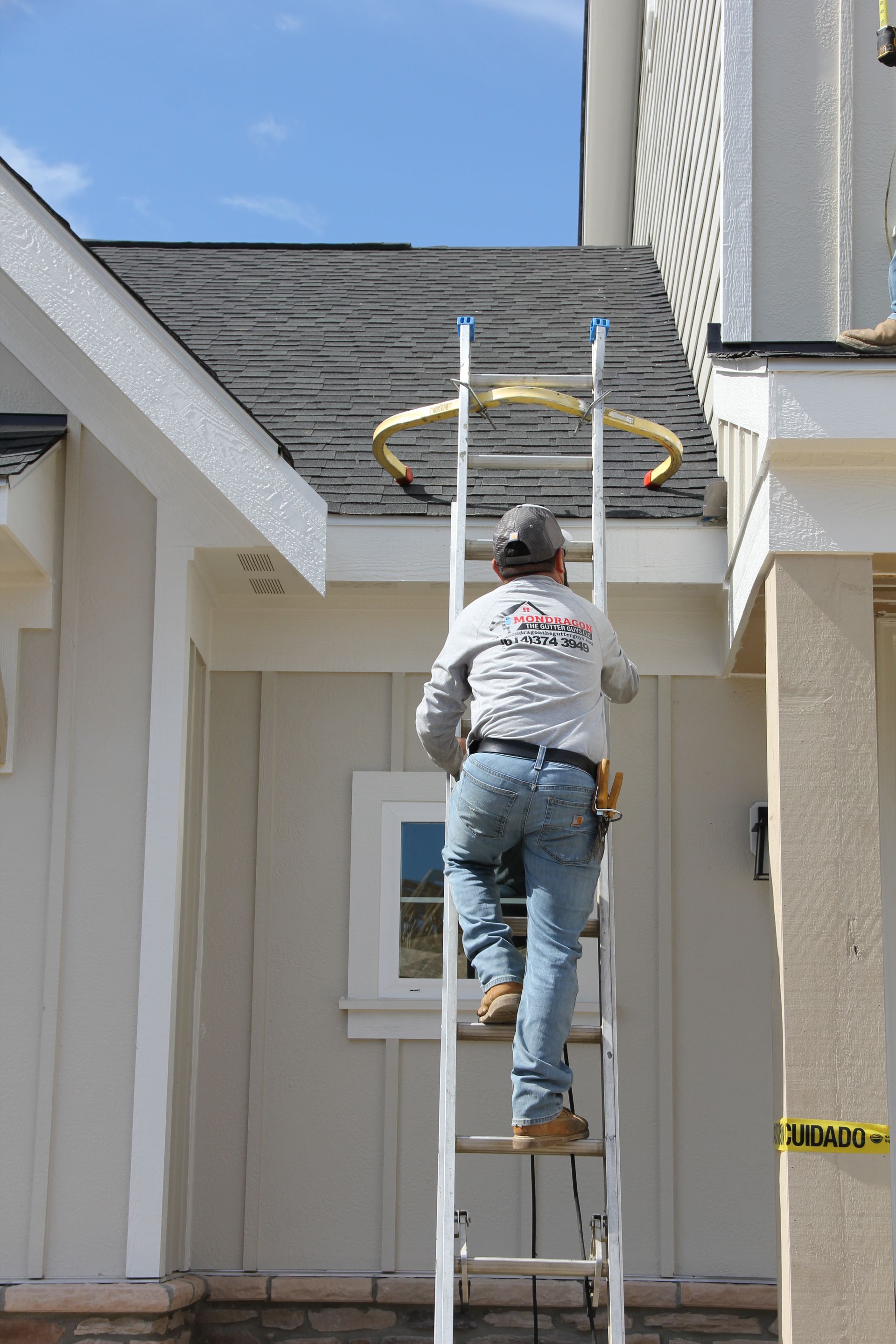 Construction worker climbing a ladder to work on a roof. Light-colored building, blue sky.