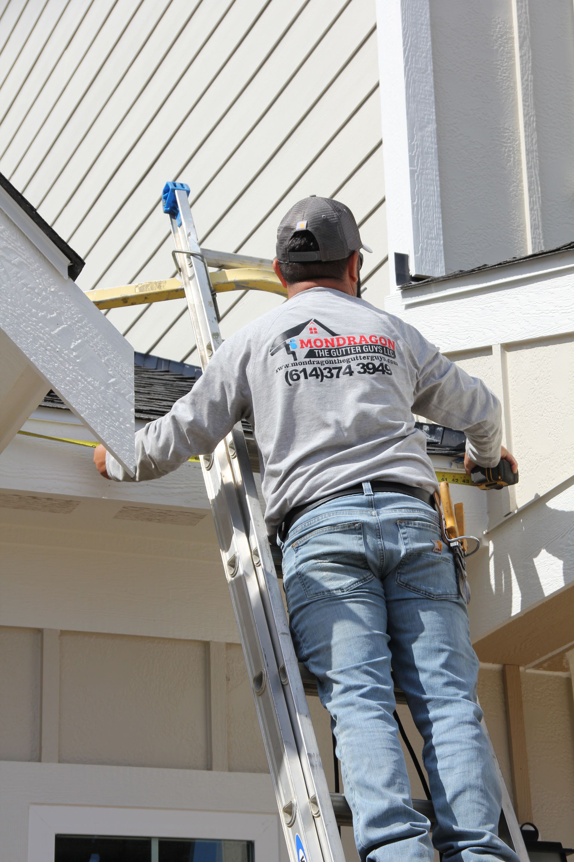 Man on ladder measuring and working on the side of a house.