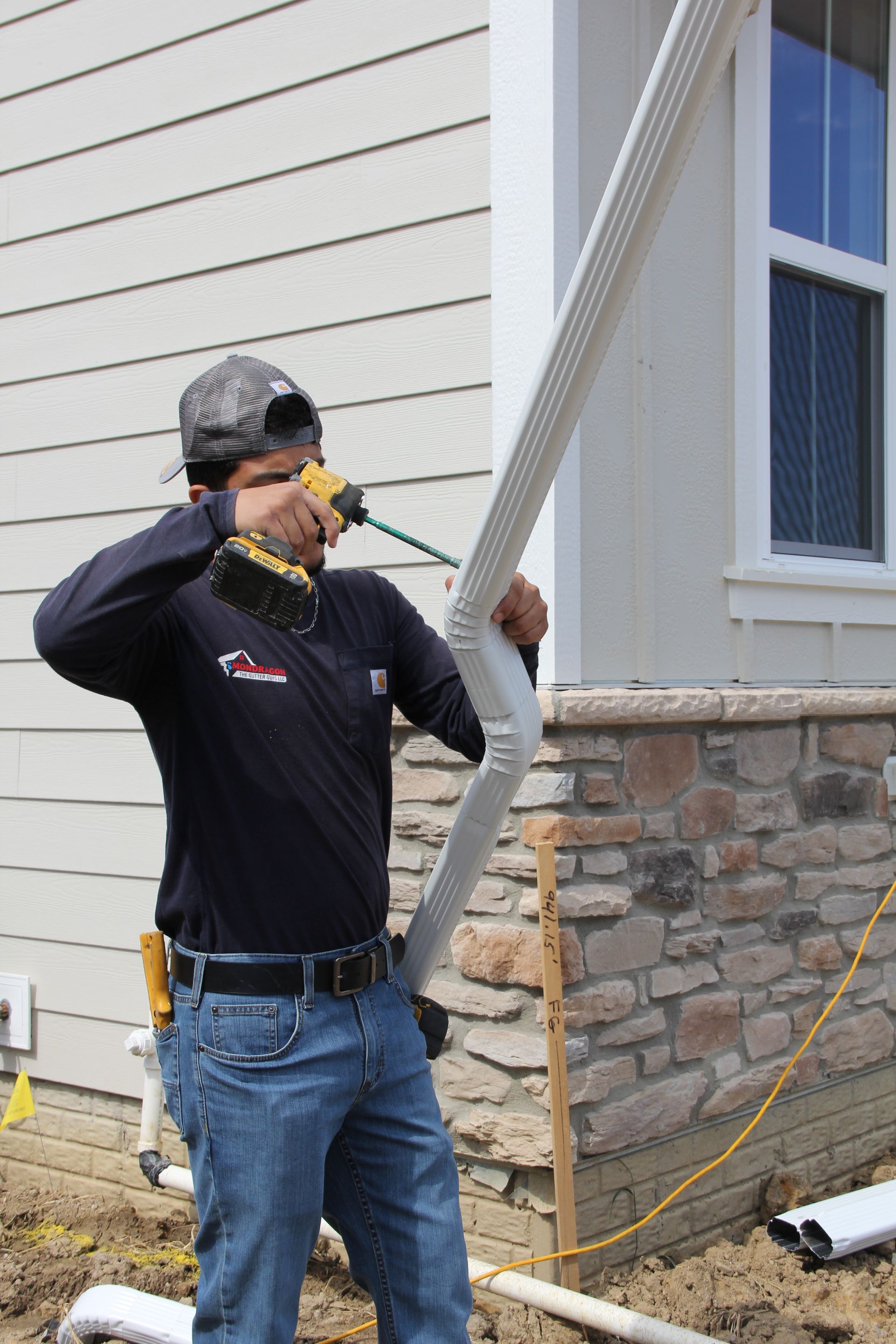 A construction worker in jeans and a hat installing a white gutter on a building.