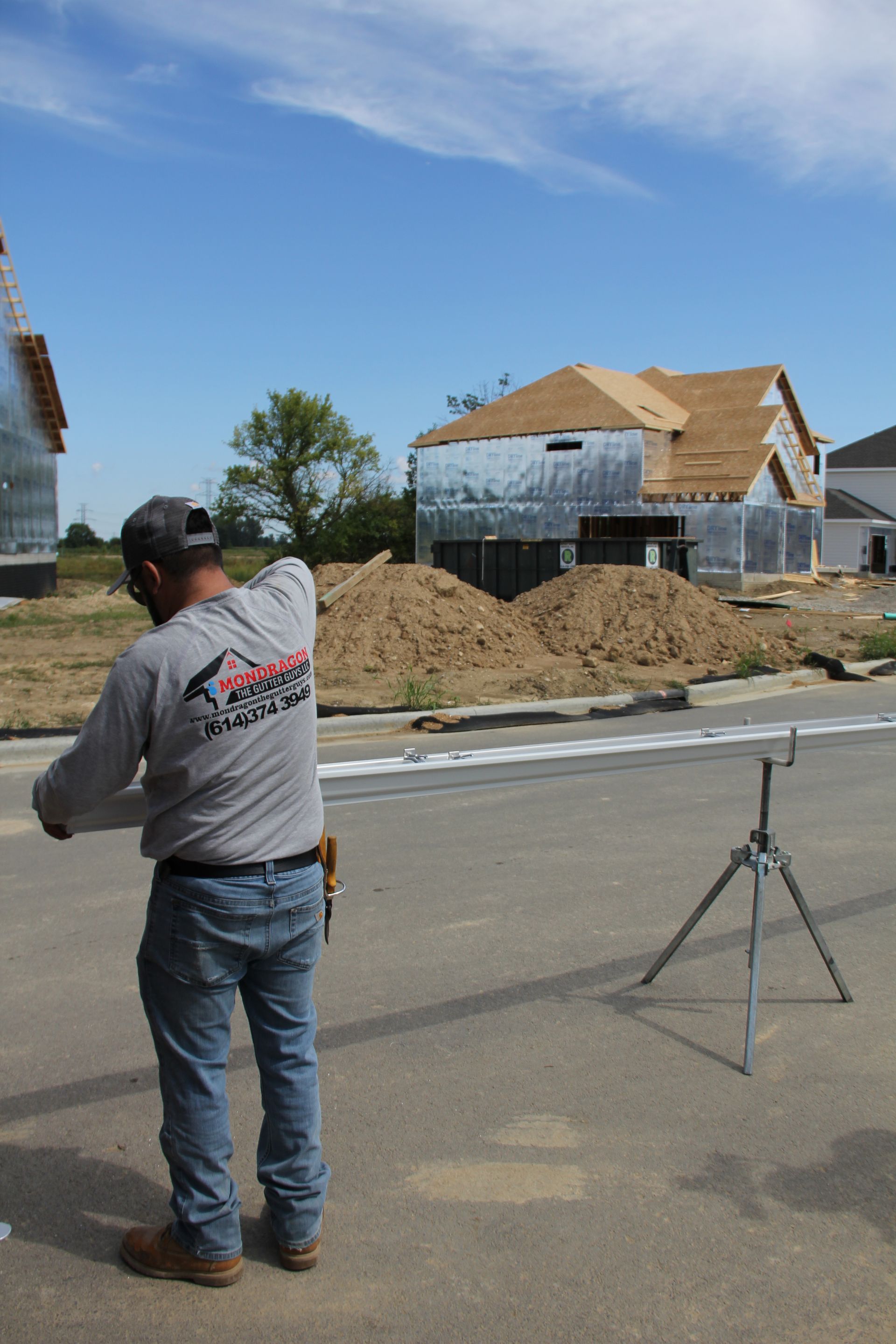 Construction worker on a street, measuring with a tripod, houses under construction in the background, blue sky.