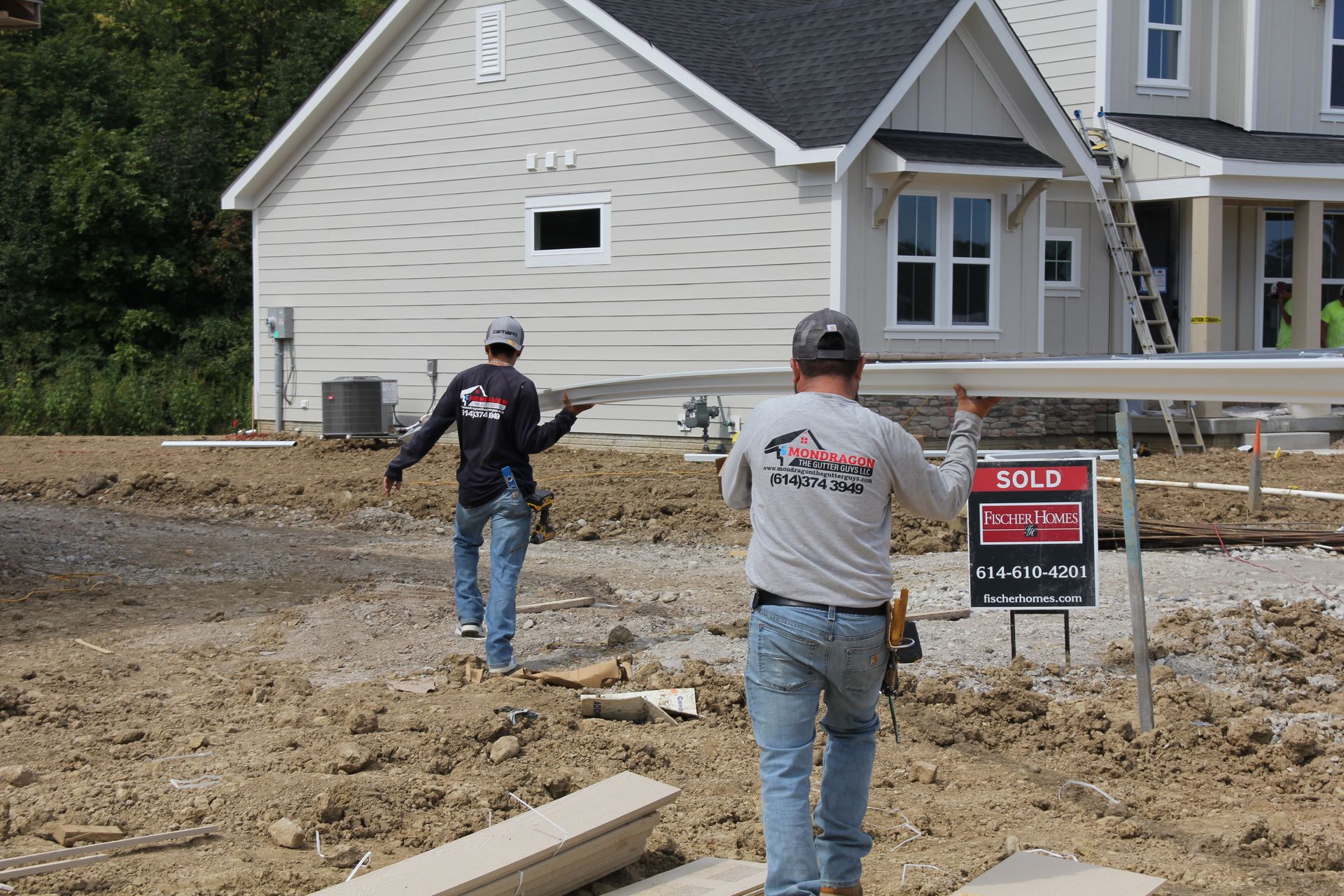 Two construction workers carrying a beam towards a newly built house; 