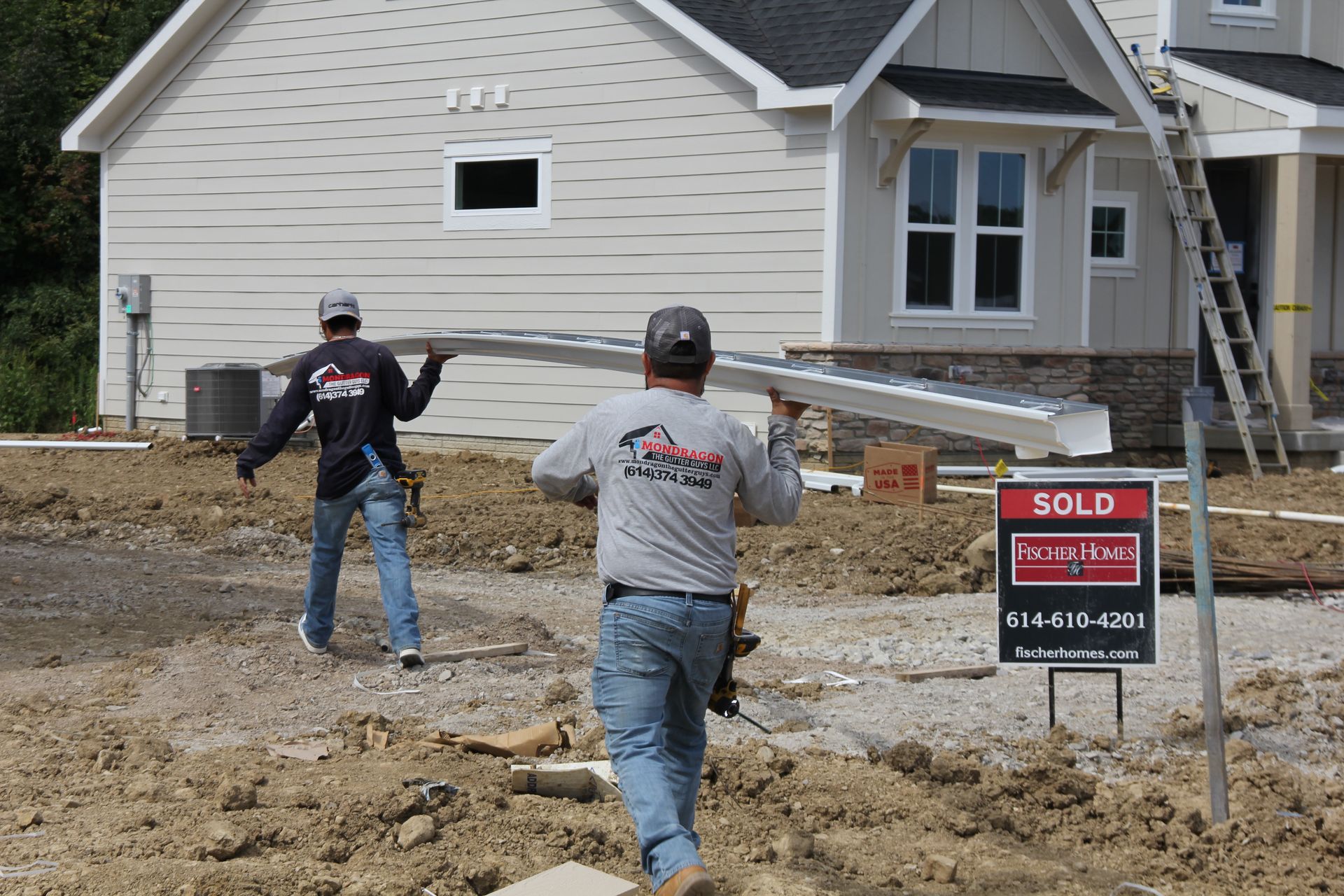 Two construction workers carry a long piece of siding toward a new house, 