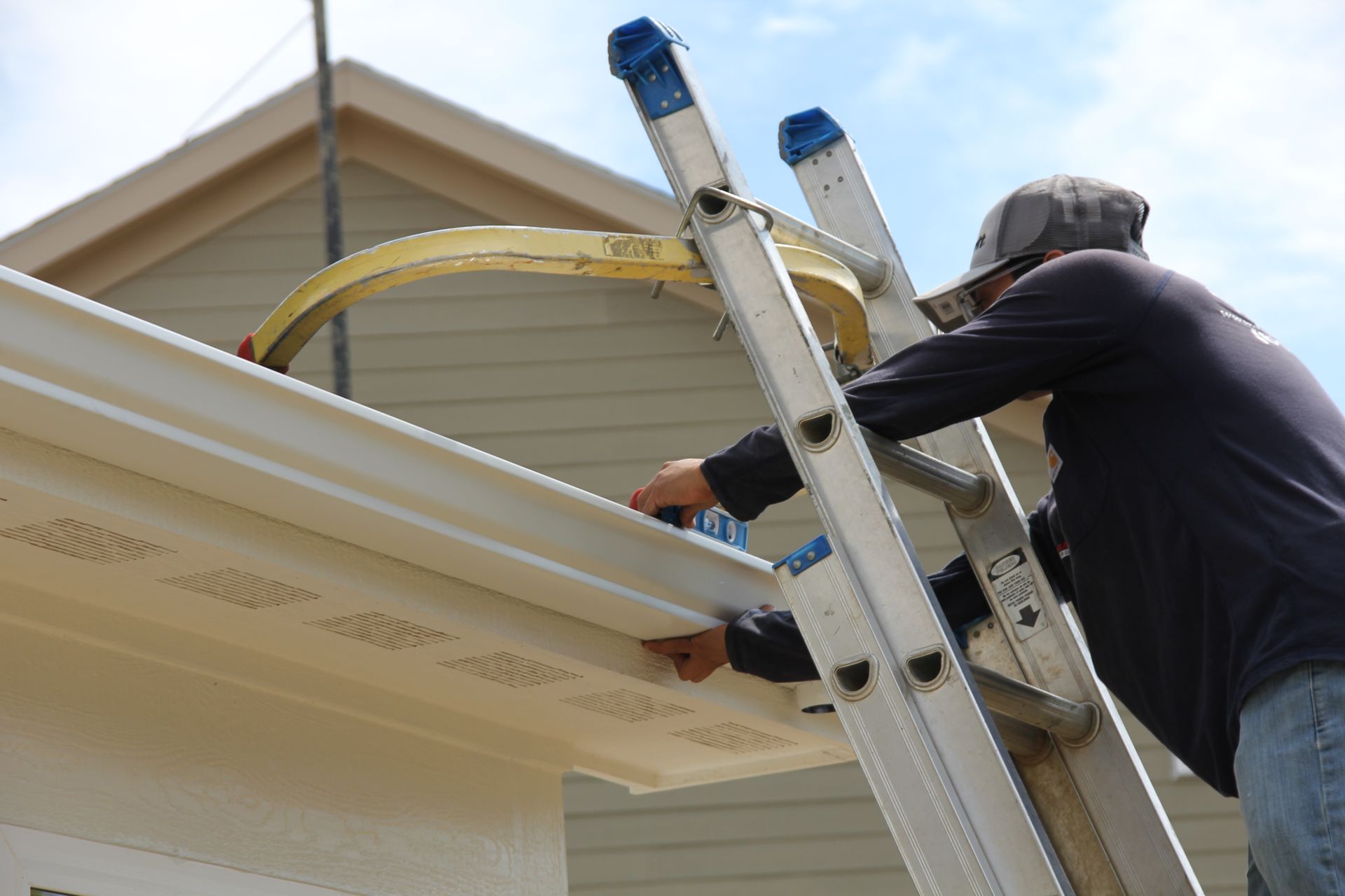 Person on a ladder installing guttering on a house, using a yellow support.