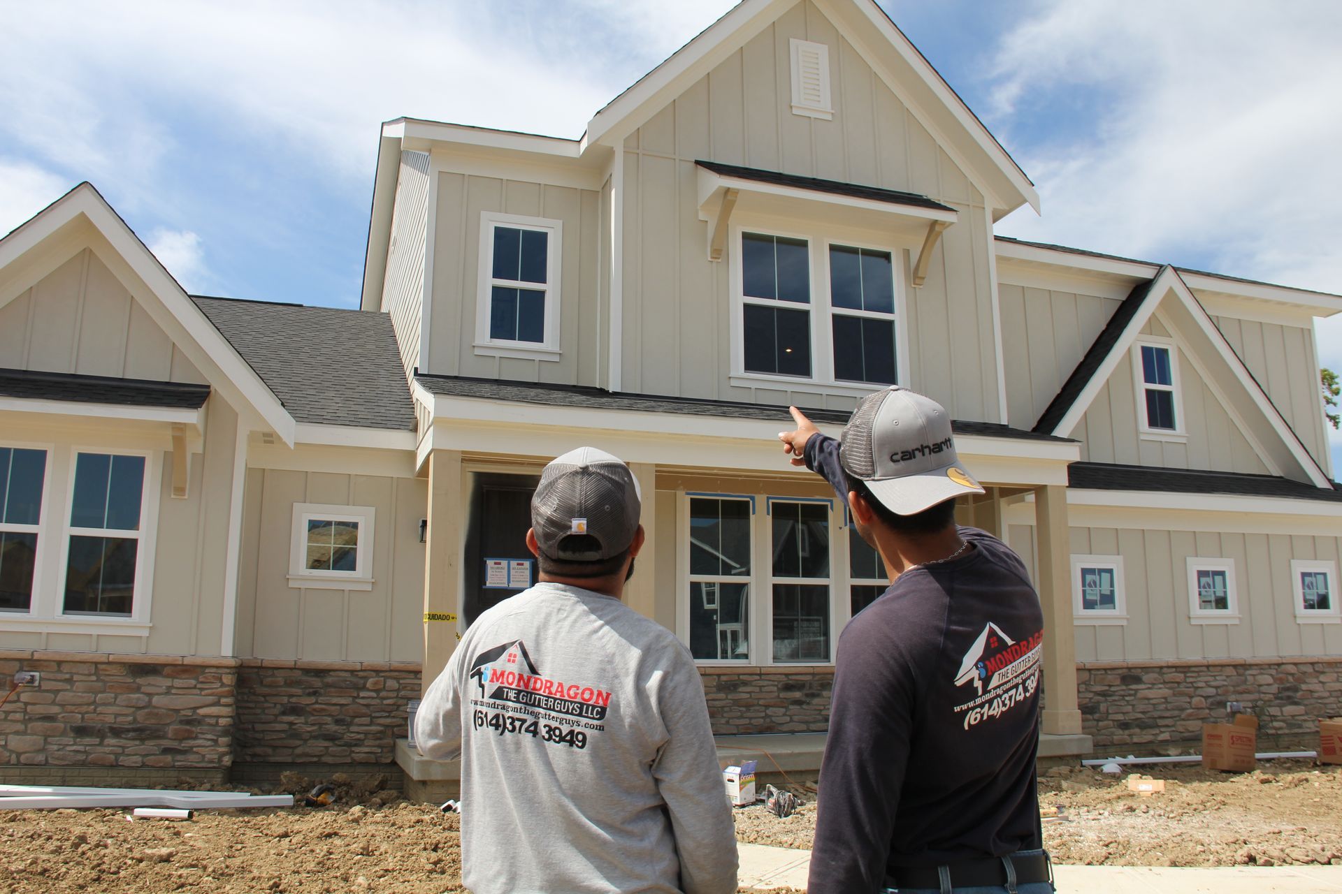 Two construction workers examining a beige house under construction; one points up.