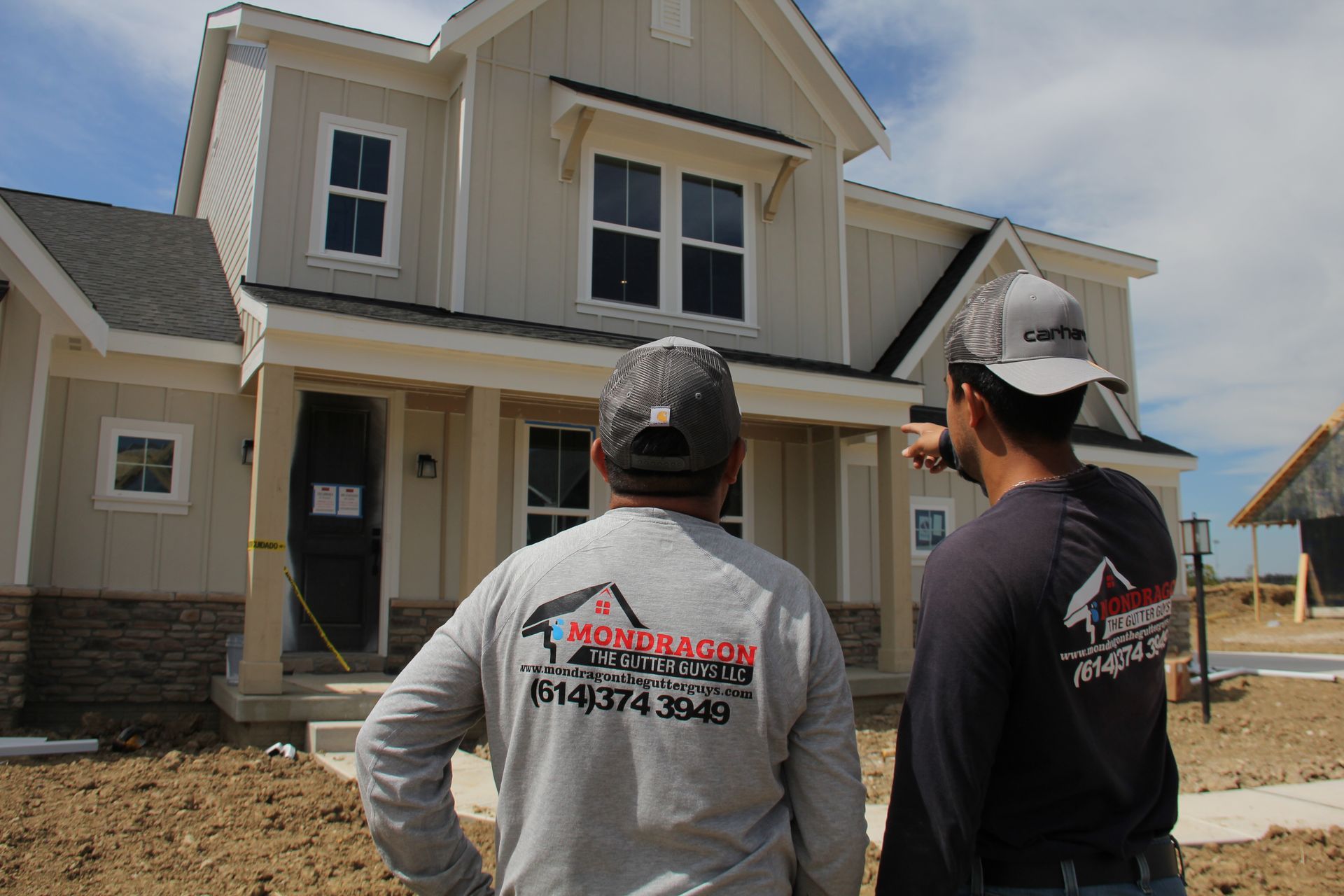 Two construction workers inspecting a beige two-story house under construction. One points, the other looks on.