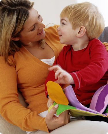 Woman in orange top smiles at child in red shirt holding a soft toy.