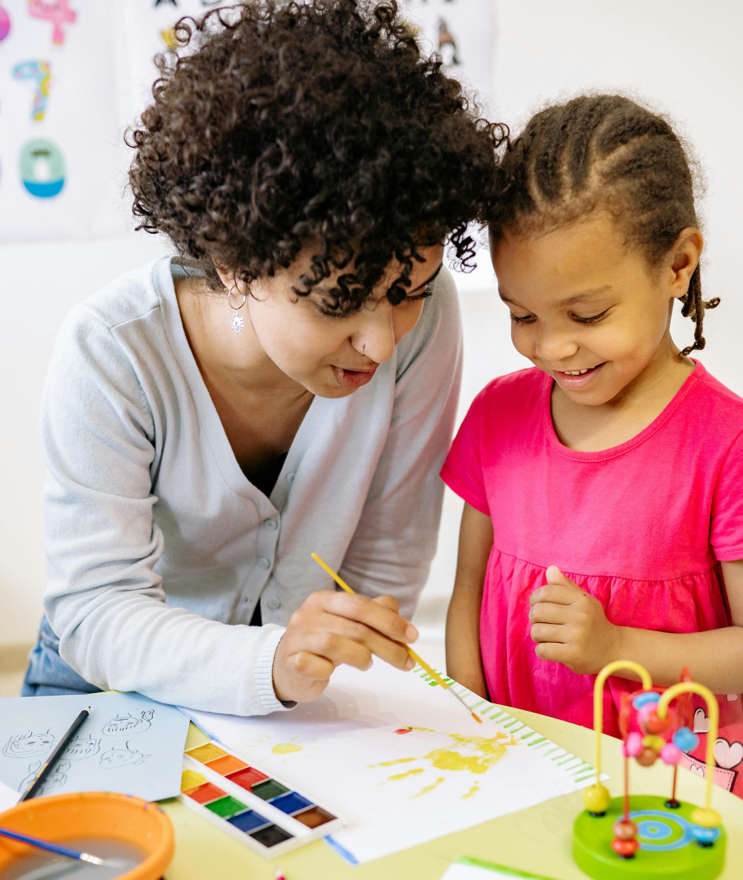 Woman and child painting together, yellow sun design on paper, bright colors.