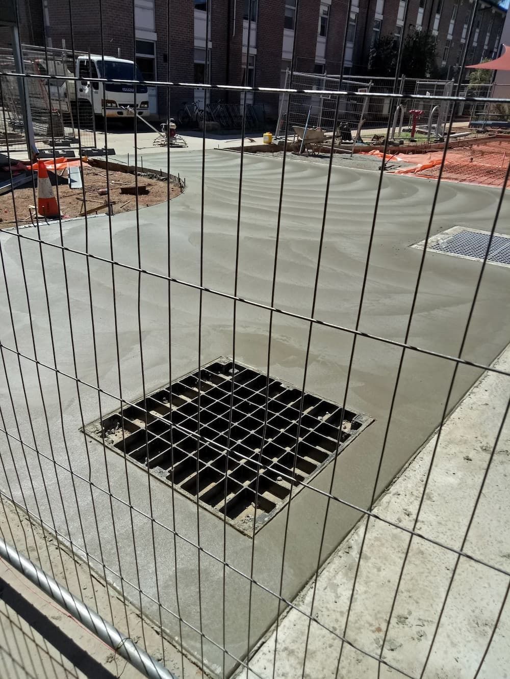 A Fence Surrounds A Construction Site With A Drain In The Middle — Heartland Concrete In Gillen, NT