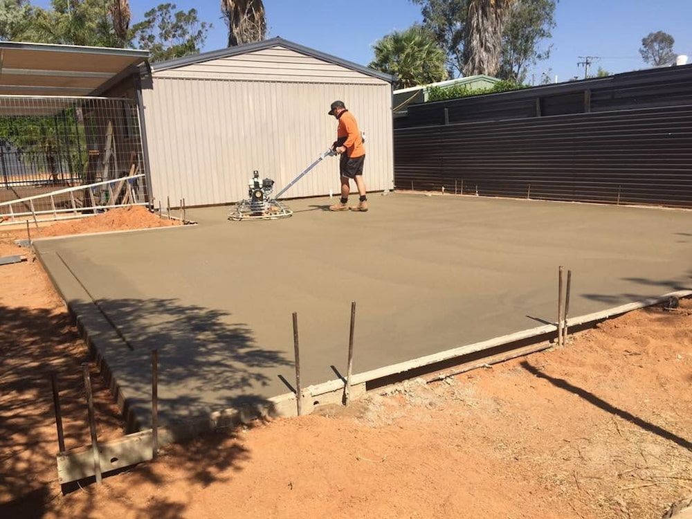 A Man Is Working On A Concrete Floor In Front Of A Shed — Heartland Concrete In Gillen, NT