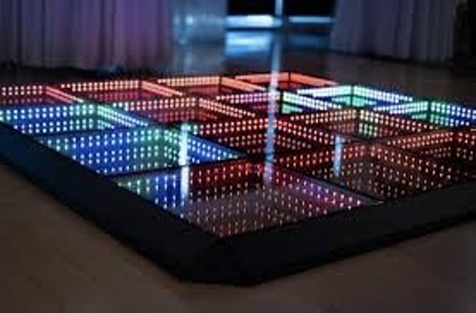 An infinity mirror LED dance floor with glowing square panels in blue, red, and green, set on a dark stage.