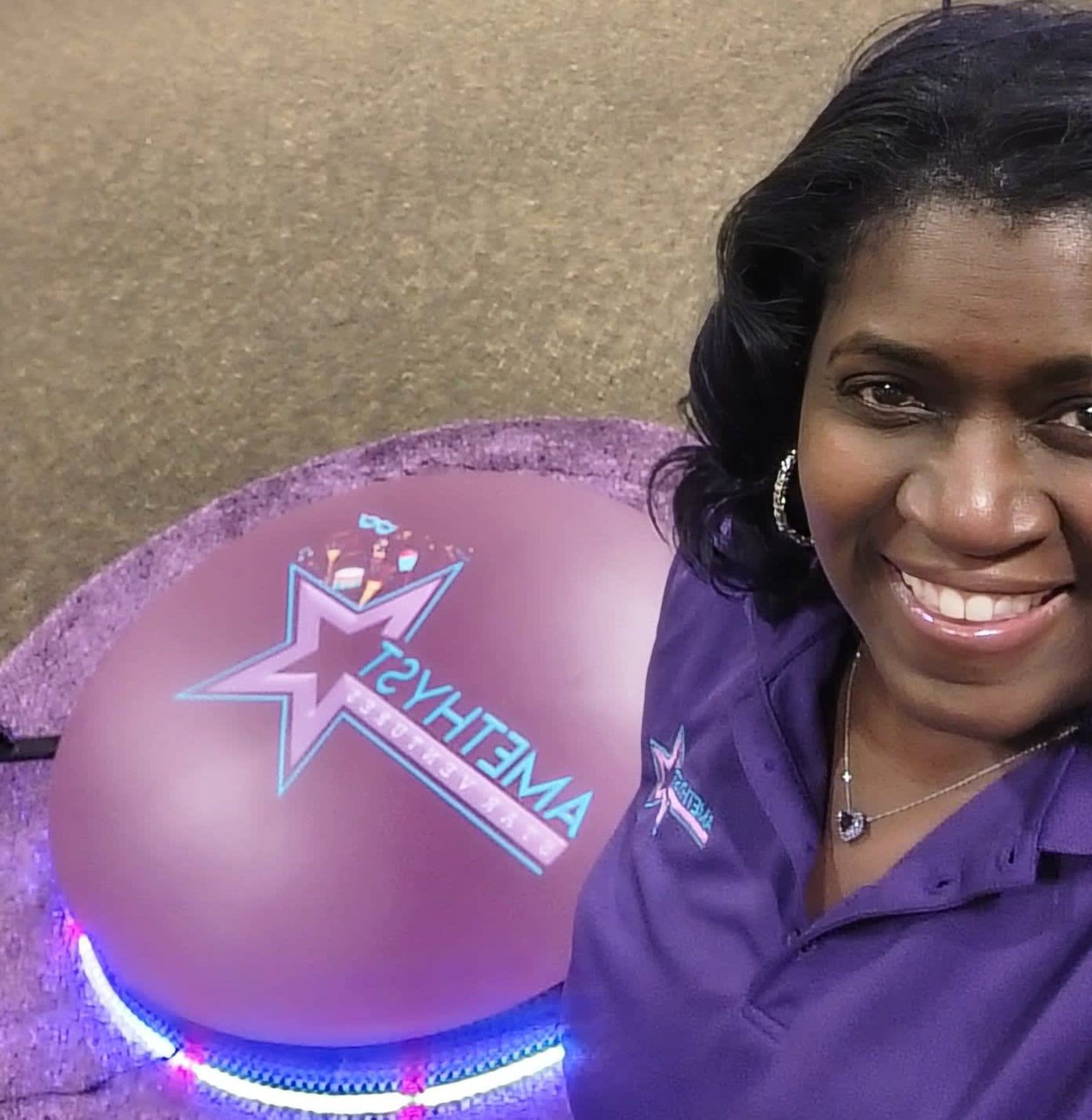 A smiling person wearing a purple shirt stands next to a circular purple platform with an Amethyst Events star logo.