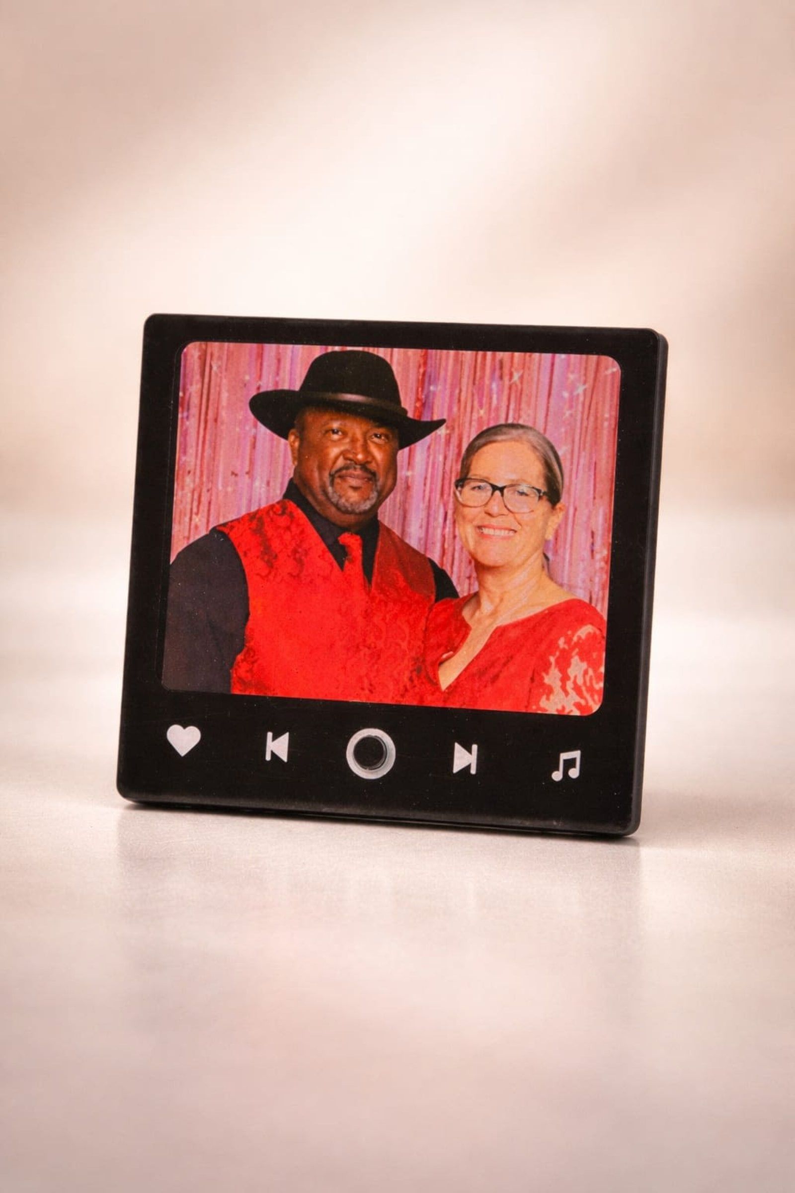 A photo frame styled as a music player features a smiling couple in red, standing against a pink backdrop.