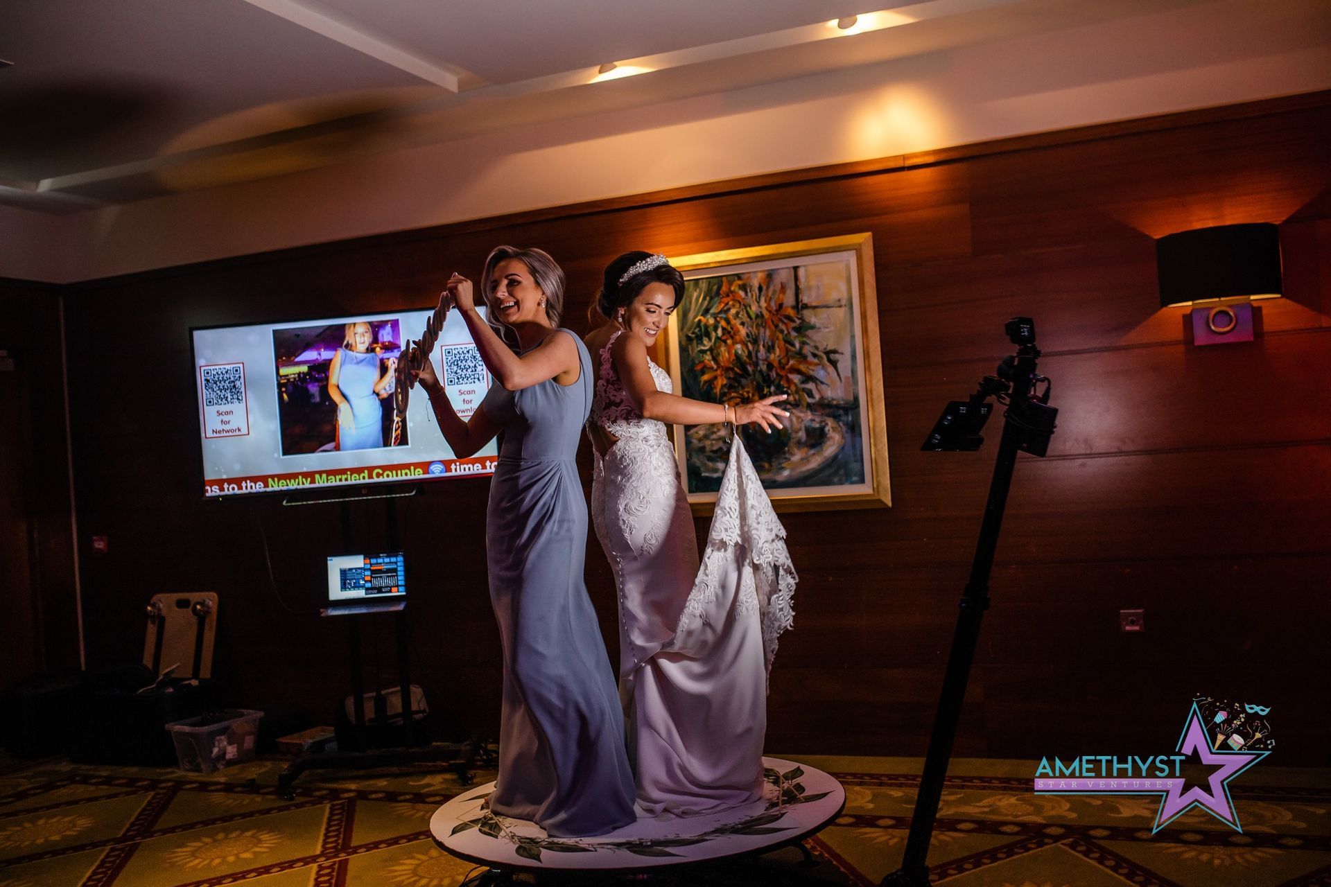 Two people in formal gowns stand back-to-back on a rotating platform in a wood-paneled room.