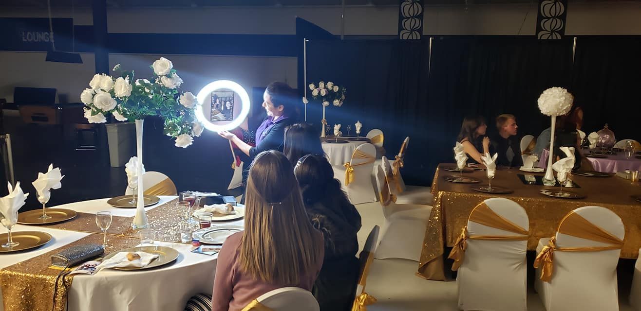 A ring light illuminates a person filming at a formal event with decorated tables and guests in a banquet hall.