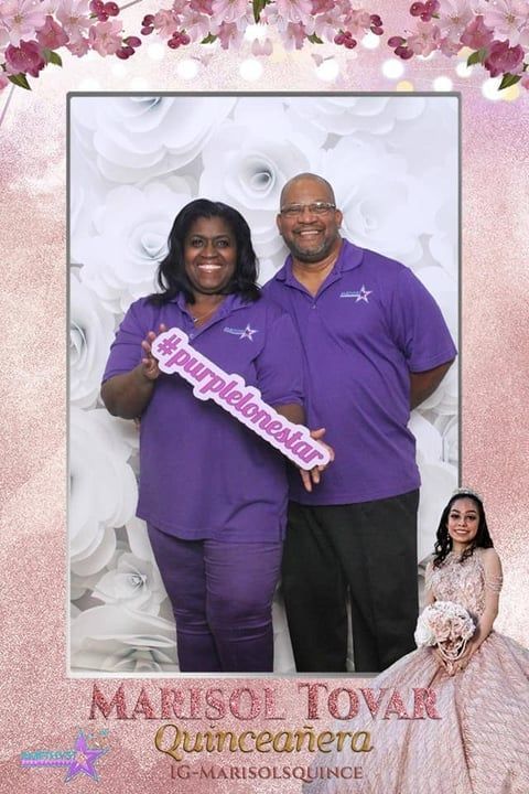 A couple in purple polo shirts holds a sign reading #purplelonestar in front of a white floral backdrop.