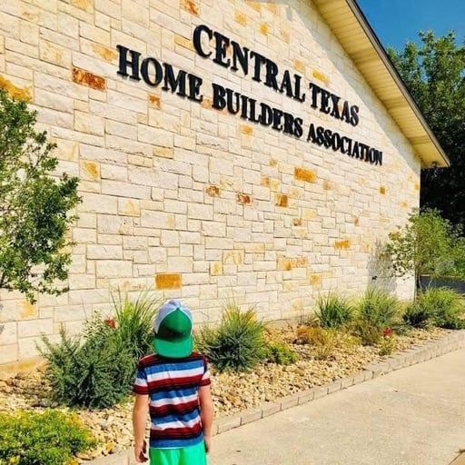 A child wearing a green hat and striped shirt stands in front of a stone building.