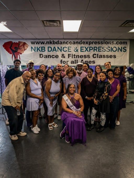 A group of people standing in front of an NKB Dance & Expressions banner, with one person seated in a purple gown.