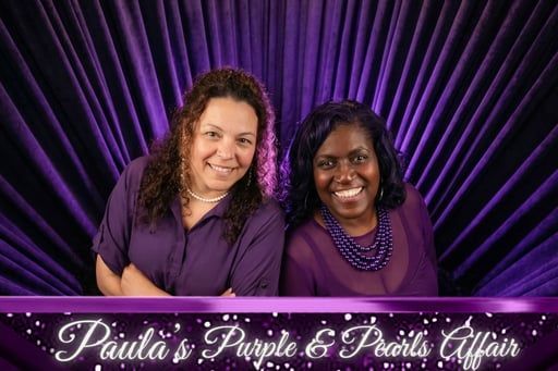 Two smiling people pose against a purple curtain backdrop.