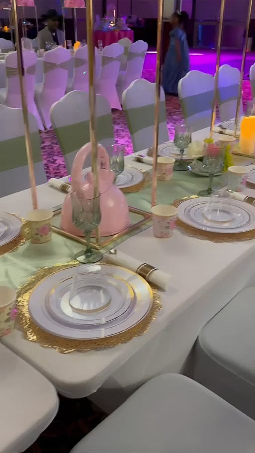 A banquet table set for a formal event with white linens, gold-rimmed plates, pink centerpieces, and tall gold stands.