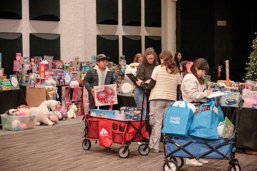 Volunteers at a toy drive fill wagons and bags with gifts in a room lined with tables of toys.