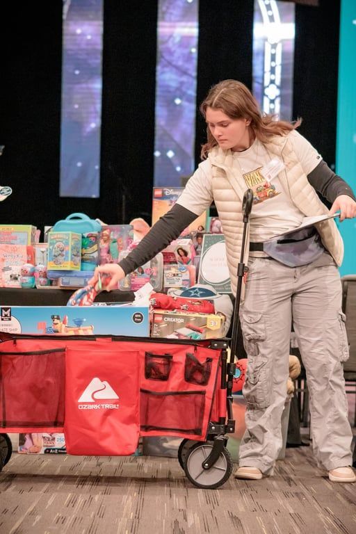 A person organizes toys into a red collapsible wagon, with shelves of additional toys and boxes in the background.