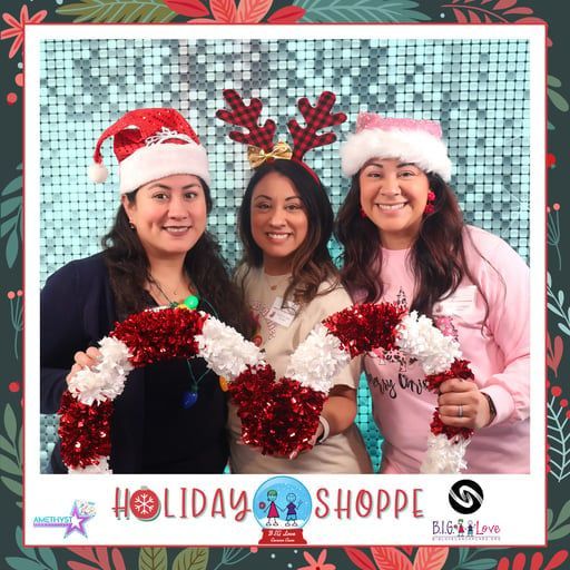 Three smiling people wear holiday hats and headbands while holding a festive garland in front of a blue sequin backdrop.